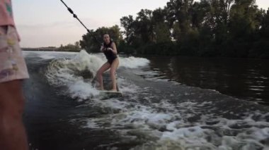 Bir ipe tutunup bir antrenörü dinlerken, bir kız nehir boyunca bir wakeboard sürüyor..