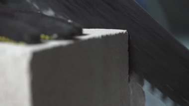 Küçük beton bloklar ve toz parçaları el testeresinin altından uçuyor. Yakın plan..