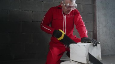 Bir adam beton bir bloğu el testeresiyle kesiyor..