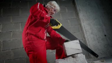 Koruyucu tulumlu bir kadın işçi binanın içinde bir testereyle tuğla keser..