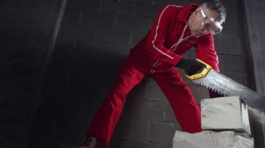 Koruyucu kıyafetli ve maskeli bir işçi beton testereyle tuğla keser..