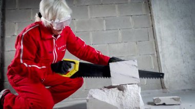 Evin içindeki bir kadın tuğla bloklarını kesmeyi ve bir parçayı diğerinden ayırmayı bitiriyor..