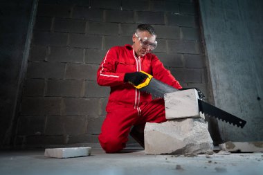 Emniyet gözlüğü takan bir adam karpit dişli bir el testeresi kullanarak beton kesiyor..