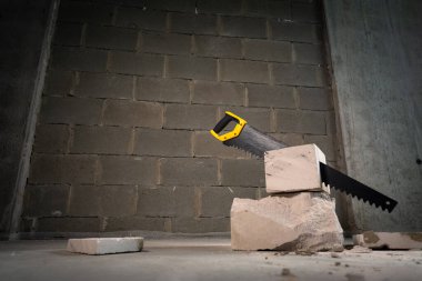 Tuğla yığınından beton çıkıntıları kesmek için bir el testeresi..