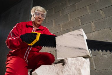 İnşaat alanında çalışan bir kadın el testeresi ile beton bloklar kesiyor..