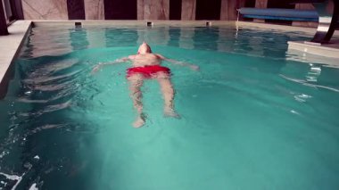Bir adam spa merkezindeki kapalı havuzda rahatça yüzüyor..