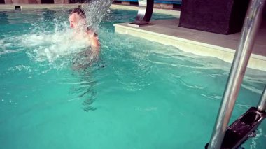 Bir adam yüzme havuzundaki şelale musluğundan akan suyun altında duruyor..