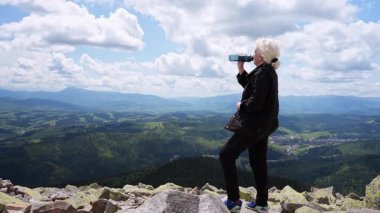 Bir kadın dağın tepesindeyken turist şişesinden su içer..