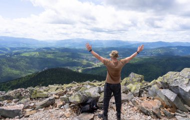 Bir adam kollarını dağların arka planına doğru açıyor, doğayı ve özgürlüğü kucaklıyor..