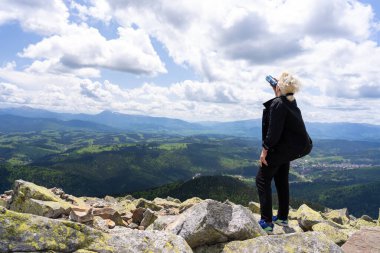 Bir kadın dağa tırmandı ve tepesinde dururken bir şişeden su içti..