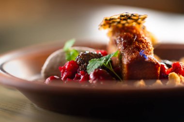 Kırmızı böğürtlenli, çırpılmış kremalı ve nane yapraklı bir tabakta çiçek yapraklarıyla süslenmiş bir ballı pasta yer alır..