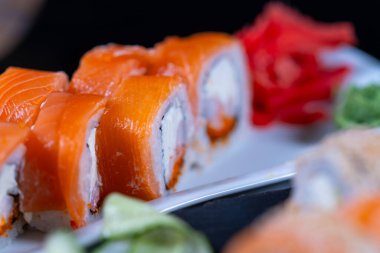 Hafif dikdörtgen bir tabakta somon, yılan balığı ve yumuşak peynirden yapılmış bir dizi suşi rulosu..