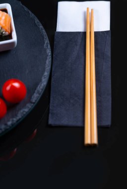 Asya çubukları, domateslerin yanında siyah beyaz bir peçete ve soya soslu bir suşi rulosunun üzerinde yatar..