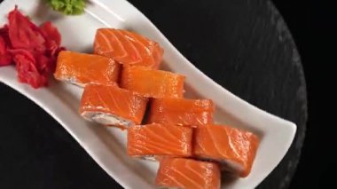 Beyaz dikdörtgen bir tabakta bir tezgahta dönen birkaç farklı suşi ruloları vardır..