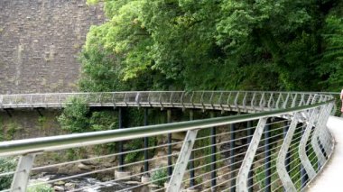 New Mills 'in Peak District kasabası Goyt nehrinin yukarısındaki Torrs Riverside Parkı' nda modern metal yaya köprüsünde yürüyen uzun kıvırcık saçlı kadının arka görüntüsü..