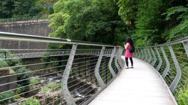 Millennium Walkway 'de yaz elbisesi giymiş bir kadın modern köprüde manzara resimleri çekiyor, New Mills, İngiltere.