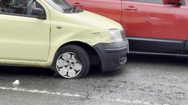 Yellow car just after the road accident on the rainy day. It hit parked stationary red car and was hit by the third vehicle which damaged front wing panel and made flat tire or tyre. Somebody moving behind the car.