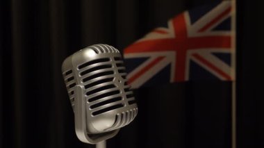 Klasik tarz gümüş renkli mikrofon yavaşça dönüyor, Büyük Britanya bayrağı perde karşısında dalgalanıyor, Eurovision Şarkı Yarışması konsepti.