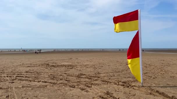 赤い黄色のライフガード旗が手を振って 広いアインズデールビーチの風に飛びますサウスポート近くの北西イングランド — ストック動画