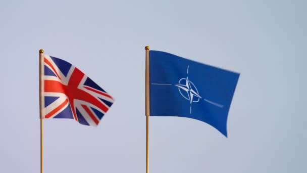 Natoとユニオンジャック 英国の国旗の隔離されたフラグは セキュリティにおけるパートナーシップのシンボル それほど白い背景ではない平原に対して手を振って 遅い動き コピースペース — ストック動画