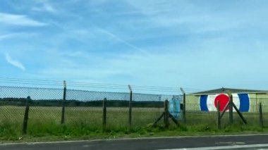 Kraliyet Hava Kuvvetleri 'nin, RAF havaalanının ve tel örgülerin arkasındaki bir binanın yanından geçiyoruz..