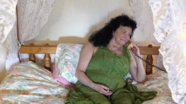 El sabit telefon ahizesi ya da cep telefonu ahizesini yeşil retro tarzı elbise ya da dört posterli yatak giyen uzun saçlı mutlu kadına veriyor. Perdenin arkasında birine gülümsüyor ve konuşurken....