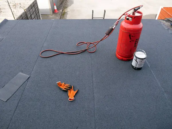 ほぼ完成した新しいビットメン屋根に立っている接続されたブローターが付いている赤いプロパンガス シリンダーは平らな屋根を覆いました ロイヤリティフリーのストック画像