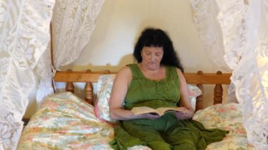 Yeşil elbiseli orta yaşlı bir kadın eski tarz paraşüt yatağında kitap okuyor..