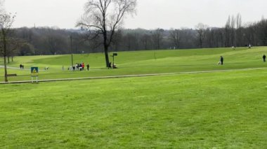 İnsanlar Manchester, Birleşik Krallık 'ın ünlü Heaton Parkı' nda bahar başlarında dinleniyorlar. Arka planda görünen uzak şehir silueti.