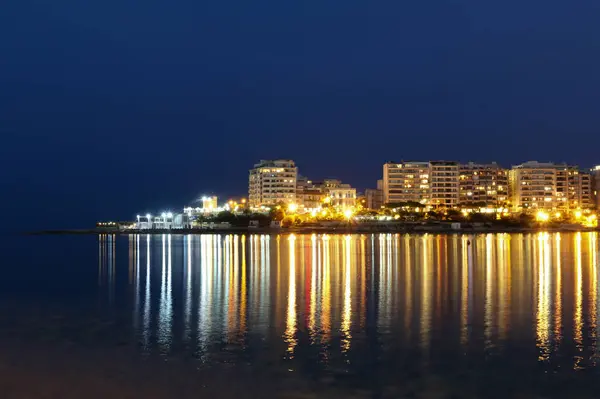Deniz kıyısındaki tatil beldesinin uzun yansımaları Akdeniz 'in sakin suları üzerindeki gece ışıkları.