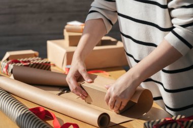 Ahşap bir masanın üzerinde el işi kağıt içinde kutu taşıyan genç bir kadın. Kutlama için hediye hazırlığı. Eko paketleme ile paketleme yeteneği.