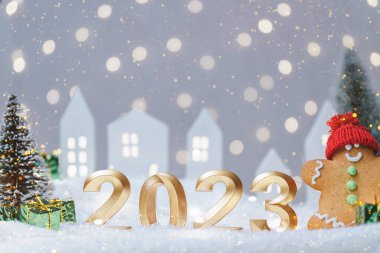 2023 yılının altın sayıları ve zencefilli kurabiye adam. Işık arka planında Bokeh olan ışıltılı bir çelenk. - Mutlu yıllar. Sıcak bir atmosfer, arka planda ağaçlar olan küçük şirin bir ev.