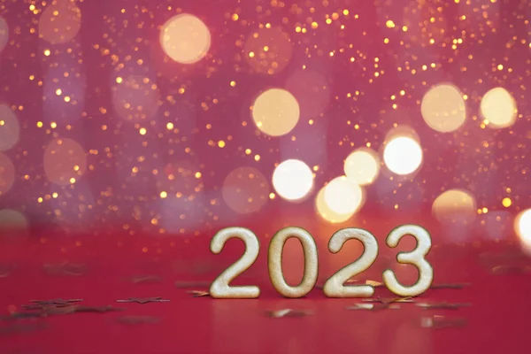 Golden numbers of year 2023. Happy New Year greeting card with copy space. . Glowing festive garland with bokeh on red background.
