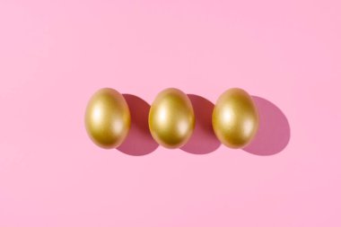 Easter template with golden eggs. Egg painted gold on pink background. Easter concept with copy space for text. Flat lay style minimalistic design.
