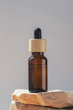 Amber dropper bottle with serum or gel on stone podium. Grey background. Beauty concept for face and body care. Skincare products, natural cosmetic.