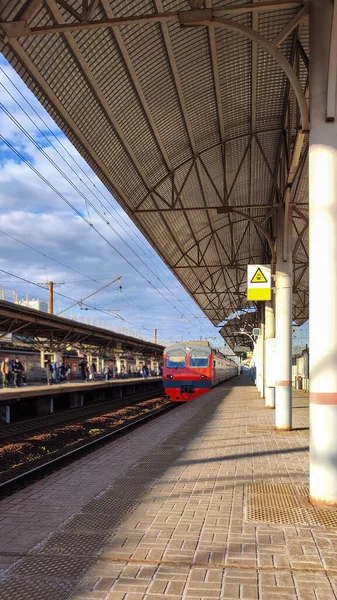到城郊列车的月台空荡荡的天台下阳光明媚的春日和云彩 橙色通勤列车迎面而来 俄罗斯城市间通信的概念 复制空间 — 图库照片