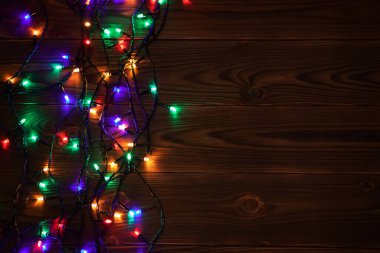 Işıklı ve bedava metin alanlı bir Noel arkaplanı. Noel ışıkları sınırda. Ahşap arka planda parıldayan renkli Noel ışıkları. Yeni yıl. Noel zamanı. Dekorasyon. Çelenk.