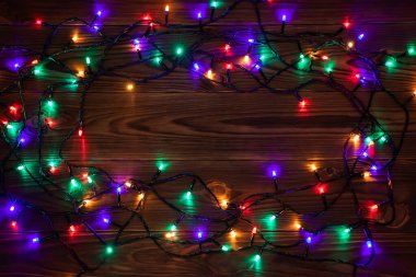 Işıklı ve bedava metin alanlı bir Noel arkaplanı. Noel ışıkları sınırda. Ahşap arka planda parıldayan renkli Noel ışıkları. Yeni yıl. Noel zamanı. Dekorasyon. Çelenk.