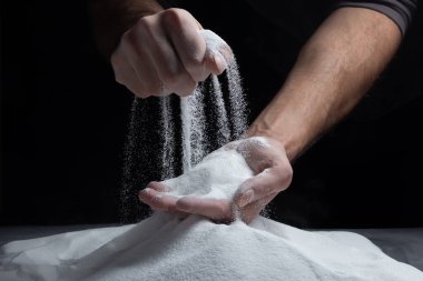 Siyah arka plandaki parmaklar aracılığıyla kum. Hayatın akışı kavramı..