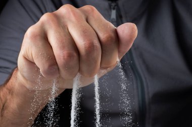 Siyah arka plandaki parmaklar aracılığıyla kum. Hayatın akışı kavramı..