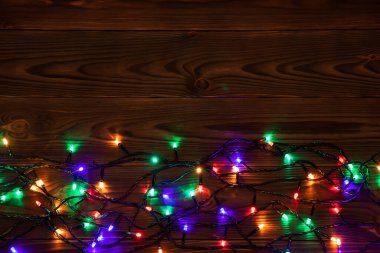 Işıklı ve bedava metin alanlı bir Noel arkaplanı. Noel ışıkları sınırda. Ahşap arka planda parıldayan renkli Noel ışıkları. Yeni yıl. Noel zamanı. Dekorasyon. Çelenk.