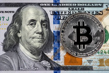 Silver symbolic coin Bitcoin on banknotes of one hundred dollars. Exchange bitcoin cash for a dollars. Cryptocurrency on US dollar bills. Digital modern method of payment. Savings, investments concept