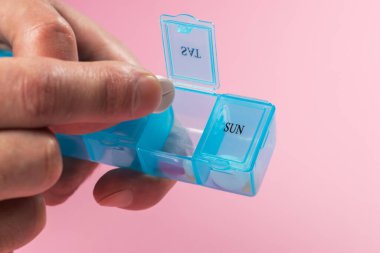 Man take pills from box. Pill organizer with variety of pills and supplement in hands. Weekly Pill Organizer on pink background. Daily pill box with medications and nutritional supplements.