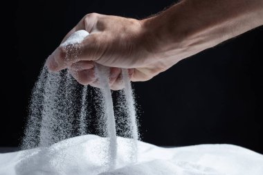 Siyah arka plandaki parmaklar aracılığıyla kum. Hayatın akışı kavramı..