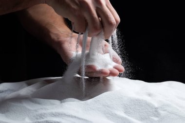 Siyah arka plandaki parmaklar aracılığıyla kum. Hayatın akışı kavramı..