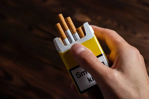 A mans hand holding out an open pack of cigarettes.