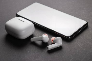 Kablosuz beyaz kulaklık, siyah arka planda çanta ve akıllı telefon..
