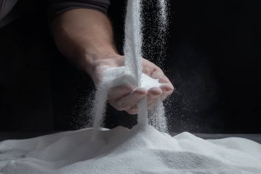 Siyah arka plandaki parmaklar aracılığıyla kum. Hayatın akışı kavramı..