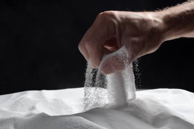 Siyah arka plandaki parmaklar aracılığıyla kum. Hayatın akışı kavramı..