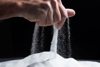 Siyah arka plandaki parmaklar aracılığıyla kum. Hayatın akışı kavramı..